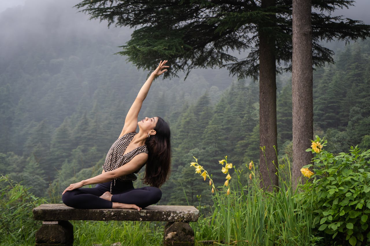 A woman performing yoga on a stone bench amidst a peaceful forest in Dharamshala, India.